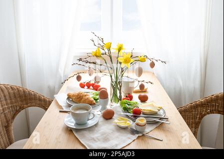 Breakfast for two with daffodils and Easter decoration on a wooden table at the window, copy space, selected focus, narrow depth of field Stock Photo