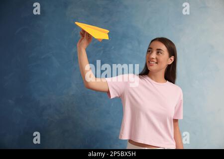 Beautiful young woman playing with paper plane on light blue background Stock Photo