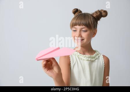 Cute little girl playing with paper plane on light grey background Stock Photo