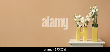 Vases in shape of word HI with beautiful eustoma flowers on table near beige wall. Banner for design Stock Photo