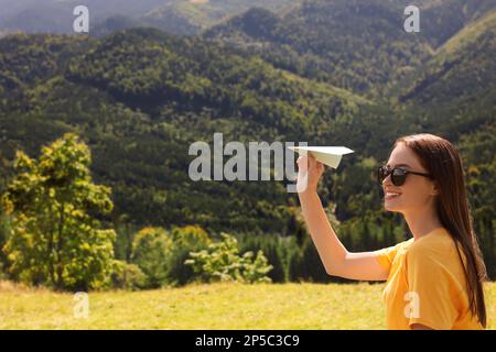 Woman throwing paper plane in mountains on sunny day. Space for text Stock Photo