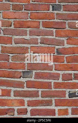 Old, red brick wall that has uneven, horizontal lines and has been weathered outdoors in New England Stock Photo