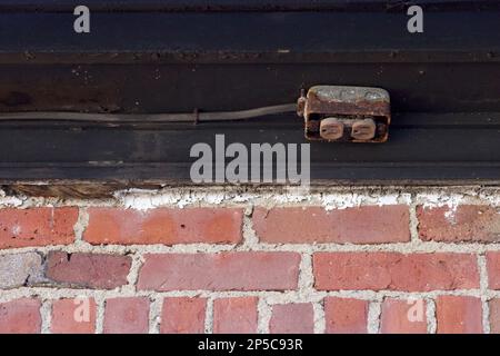 Red brick wall with black trim on top, that has rusted electrical outlet installed on the trim.  Weathered from being outdoors in New England. Stock Photo