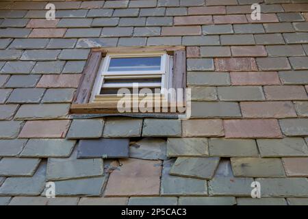 Slate siding tiles on the wall of a building in New England. There is a window in the middle with broken tiles falling apart below it. Stock Photo