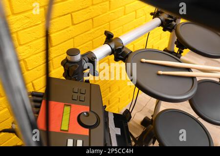 Modern electronic drum kit near yellow brick wall indoors. Musical instrument Stock Photo