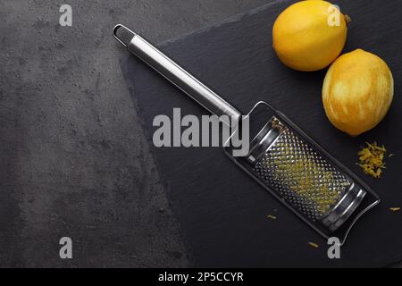 Grater and fresh lemons on black table, flat lay. Space for text Stock Photo