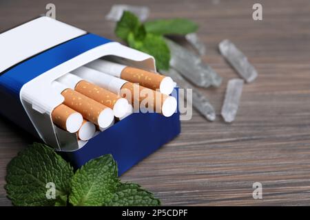 Pack of cigarettes, menthol crystals and mint on wooden table, closeup.  Space for text Stock Photo