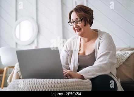 Smiling middle aged plus size woman working on laptop from home Stock Photo