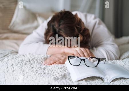 Sleeping middle aged woman withbook lying on bed at home Stock Photo