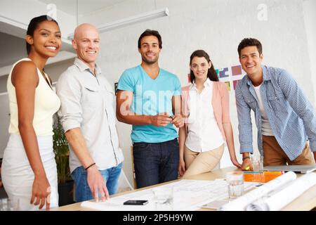 Friendly and focused. Portrait of a group of smiling designers gathered together around an office table to discuss their plans. Stock Photo