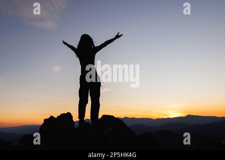 Silhouette of woman on top of the mountain looking to the sun, freedom, pray on top of mountain. Stock Photo