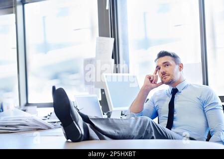 Considering his future in the company. a thoughtful-looking businessman sitting with his feet up on his desk. Stock Photo