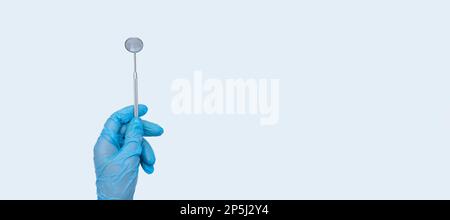 Female doctor dentist hand in blue gloves holds dentist mirror. Light background Stock Photo