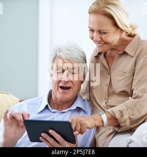 Omg, it did not just do that...a happy elderly couple using a digital tablet together at home. Stock Photo