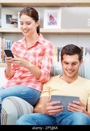 Always online. An attractive young couple relaxing at home while using their digital devices. Stock Photo