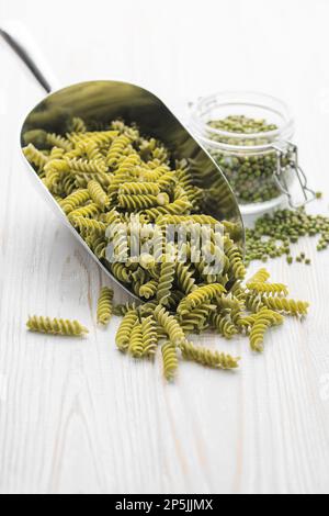 Mung bean fusilli pasta on a wooden background. Scoop with raw pasta and green mung bean. Gluten free pasta. Stock Photo