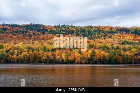 Peak fall foliage in New England. Autumn lake scene with vibrant foliage reflected on the glittering waters of Wyman Lake, on Kennebec River, Maine. Stock Photo
