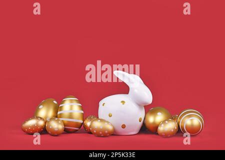 Golden Easter eggs painted with stripes and dots and bunny on red background with copy space Stock Photo