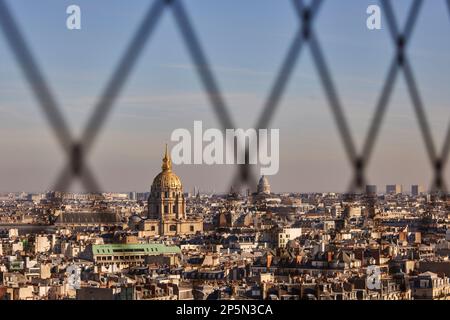 Paris landmark, rooftops framing the golden dome of Les Invalides and Napoleon’s tomb through the mesh of Eiffel Tower Stock Photo