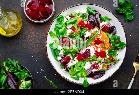 Beet, cheese and orange healthy salad with arugula, lamb lettuce, red onion, walnut and tangerine, brown kitchen table. Fresh useful dish for healthy Stock Photo