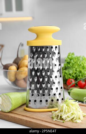 Grater and fresh zucchini on white table in kitchen Stock Photo