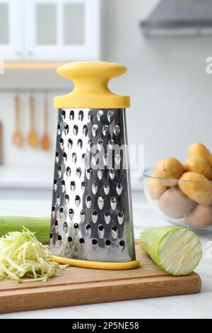 Grater and fresh zucchini on white table in kitchen Stock Photo