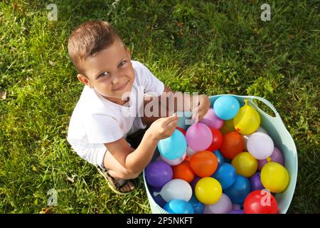 Little boy with basin of water bombs on green grass, top view Stock Photo