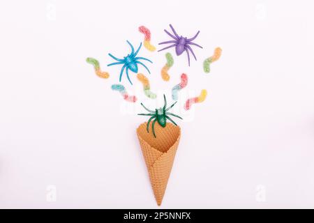 Halloween concept. Multicolored spiders, jelly candy worms and an ice cream cone on a white background. Flat lay, copy space, minimalism. High quality Stock Photo