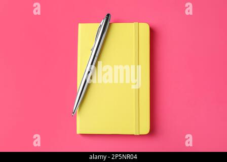 New stylish planner with hard cover and pen on pink background, top view Stock Photo