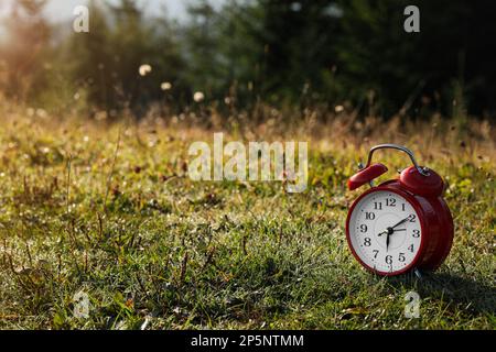 Red alarm clock on grass outdoors in morning, space for text Stock Photo