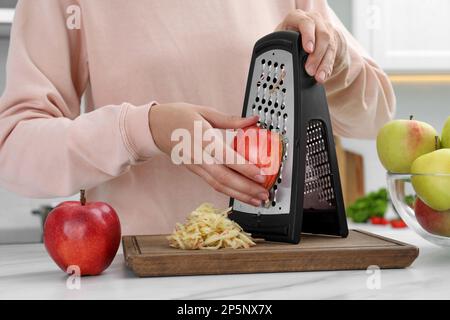Woman grating fresh red apple at kitchen table, closeup Stock Photo
