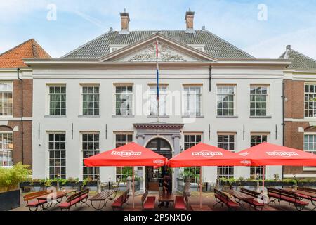 Amsterdam, Netherlands - 10 April, 2021: some tables and umbrellas in front of a large white building with two red umbrellas hanging from the roof Stock Photo