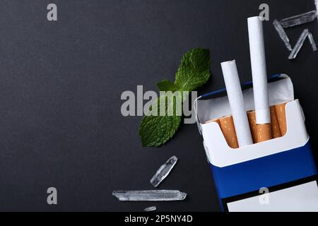 Pack of cigarettes, menthol crystals and mint on black background, flat  lay. Space for text Stock Photo
