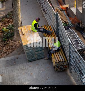 Barcelona,Spain-February 22,2023:Two construction workers check their smartphones while taking a break at a construction site. Stock Photo
