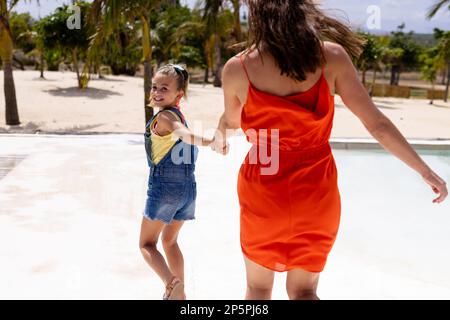 Happy biracial mother and daughter walking and holding hands at beach Stock Photo