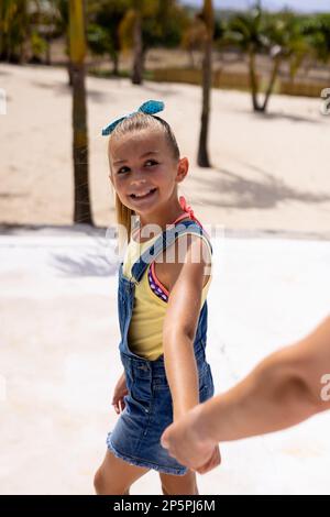 Happy biracial mother and daughter walking and holding hands at beach Stock Photo