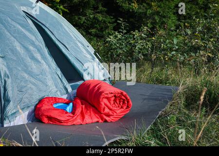 Red sleeping bag near camping tent on green grass outdoors, space for text Stock Photo