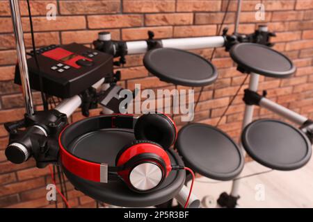 Modern electronic drum kit with headphones near red brick wall indoors. Musical instrument Stock Photo