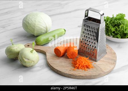 Grater and fresh vegetables on white marble table Stock Photo