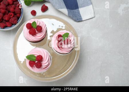 Delicious cupcakes with cream and raspberries on light grey marble table, flat lay. Space for text Stock Photo