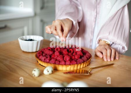 Close-up of woman's hands decorating raspberry tart, cooking delicious cake with fresh berries Stock Photo