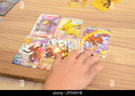 Arahal. Seville. Spain. 1st March 2023. Detail of a child's hands placing rare collectible Pokemon trading cards on a wooden table. Collectible tradin Stock Photo