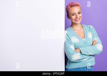 Photo portrait of satisfied smiling woman dyed pink hair folded arms wear blue print cardigan near paper banner isolated on violet color background Stock Photo