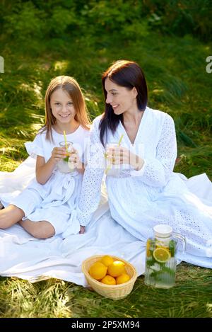 child girl child and woman holding glass of lemonade in hands and drinks on picnic Stock Photo