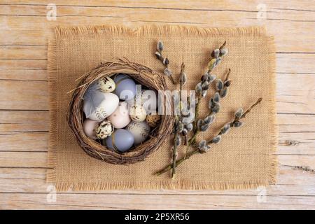 Easter eggs in nest on the sackcloth with willow twigs. Easter festive background. Top view, flat lay. Stock Photo
