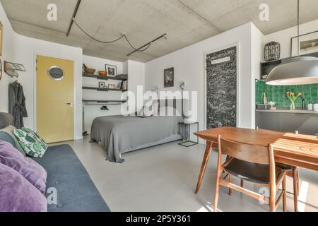 a bedroom with a bed, desk and chair in the corner next to the room's kitchen area on the right side Stock Photo