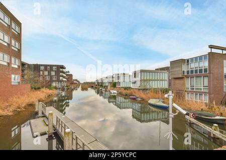 Amsterdam, Netherlands - 10 April, 2021: some houses and boats in the water with blue skies above them, as seen from an overcasted view Stock Photo