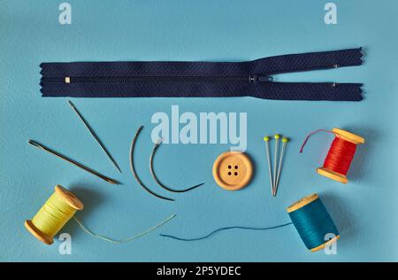 Sewing accessories - needles, thread, pins, and zipper on blue background Stock Photo