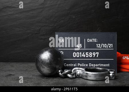 Metal ball with chain, prison uniform and mugshot letter board on grey table Stock Photo