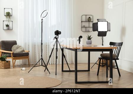 Camera and lighting equipment on tripods near table in room. Blogger workplace Stock Photo